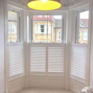 shutters—cafe-style cafe style shutters an image of cafe style shutters in white fitted into a 3 section bay window. Through the top section of the window which is not shuttered you can see light yellow coloured brick built houses