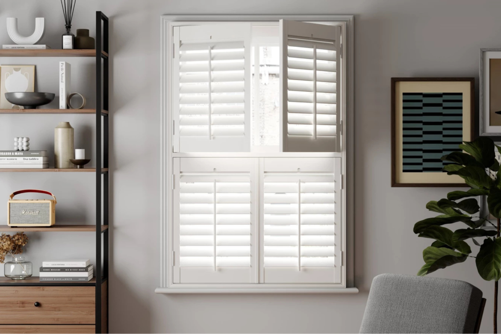 ni1 Tier on Tier Shutters - a photo of a window with a window with white tier on tier shutters, a wall unit along side with shelves and a photo, chair also visible