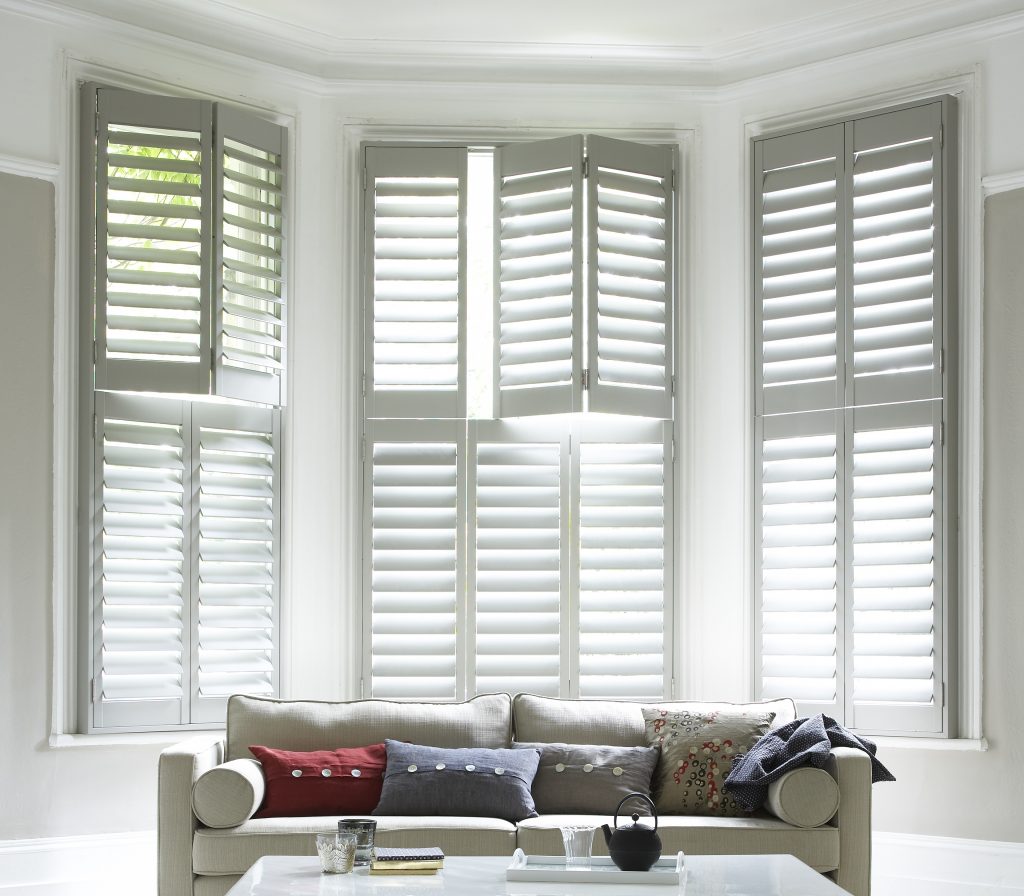 Bay Window Shutters (1) fitted bay window shutters in white above 4 seater sofa with cushions in a white room