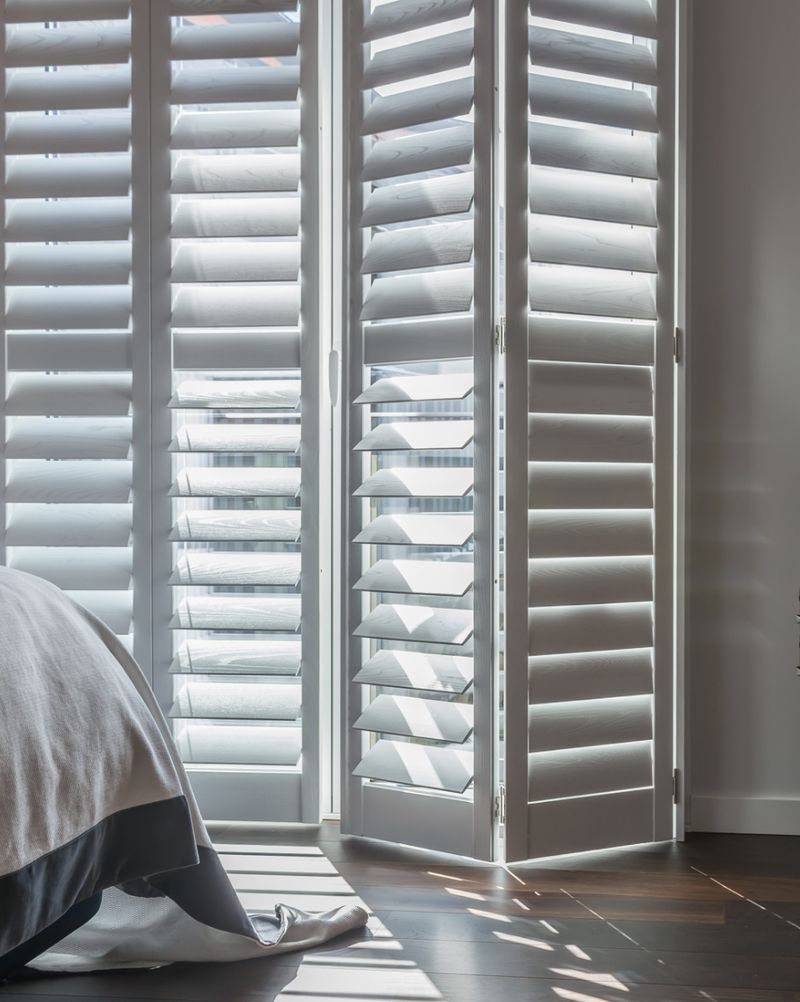 shutters in east sussex - an image of white door shutters, one is slightly bent as though the shutter is partially opened