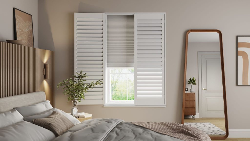 Shutters with blinds (1) a bedroom with faux wood shutter blinds -image of a bedroom with bed, a tall floor mirror you can see the reflection of the door and a chest of drawers with a white vase on it. there is also a white rug with grey zig zag pattern on it.