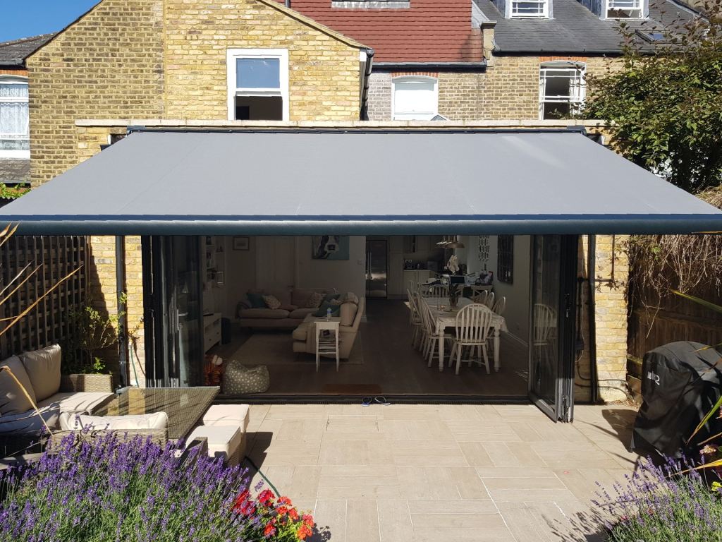 awning 1 large grey awning extended from the rear of a home, bifold door are completely open creating a flow from the living room to the outside patio area.
